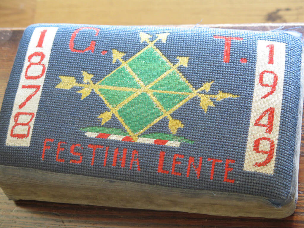 besticktes Kissen mit Wappen drauf und der Text: Festina Lente