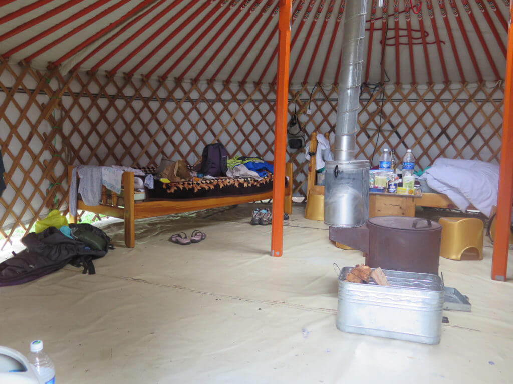 Jurte in der Mongolei innen, ein Ofen mit Rohr nach außen in der Mitte, zwei Betten und viel Gepäck