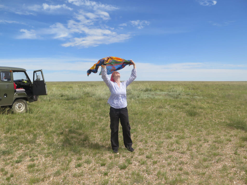 Links ein russischer Bus, blauer Himmel und Gras, Frau spielt mit Tuch im Wind