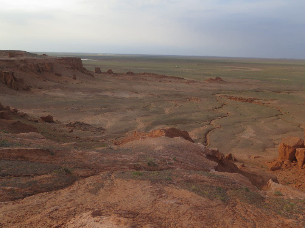 Rote Klippen Bayanzag in der Mongolei, dahinter Steppenlandschaft